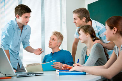Fünf Schülerinnen und Schüler befinden sich an einem Tisch im Klassenzimmer. Alle Blicke sind auf eine Person gerichtet.