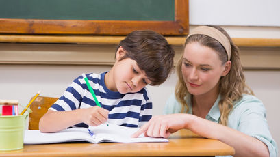 Ein Schüler schreibt in ein Heft. Die Lehrerin zeigt in das Heft.