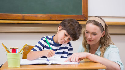 Ein Schüler schreibt in ein Heft. Die Lehrerin zeigt in das Heft.
